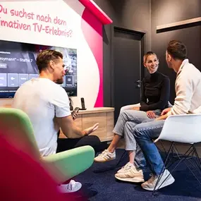 Drei Personen im Büro besprechen TV-Streaming am Bildschirm in Lounge-Ecke