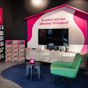 TV-Ausstellungsraum mit Fernseher, grüner Lounge, Regal und Werbetext