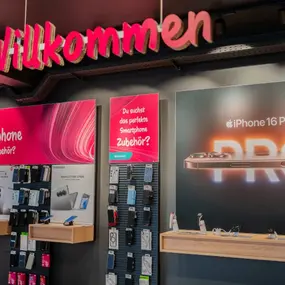 Smartphone-Shop mit Willkommensschild, iPhone 16 Pro Werbung und Handy-Zubehör an der Wand.