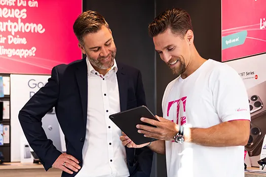 Telekom Mitarbeiter zeigt Tablet im Smartphone-Shop, zwei Männer lächeln