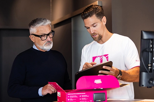 Mitarbeiter erklärt Tablet, Kunde prüft Magenta-Produkt im Telekom-Shop